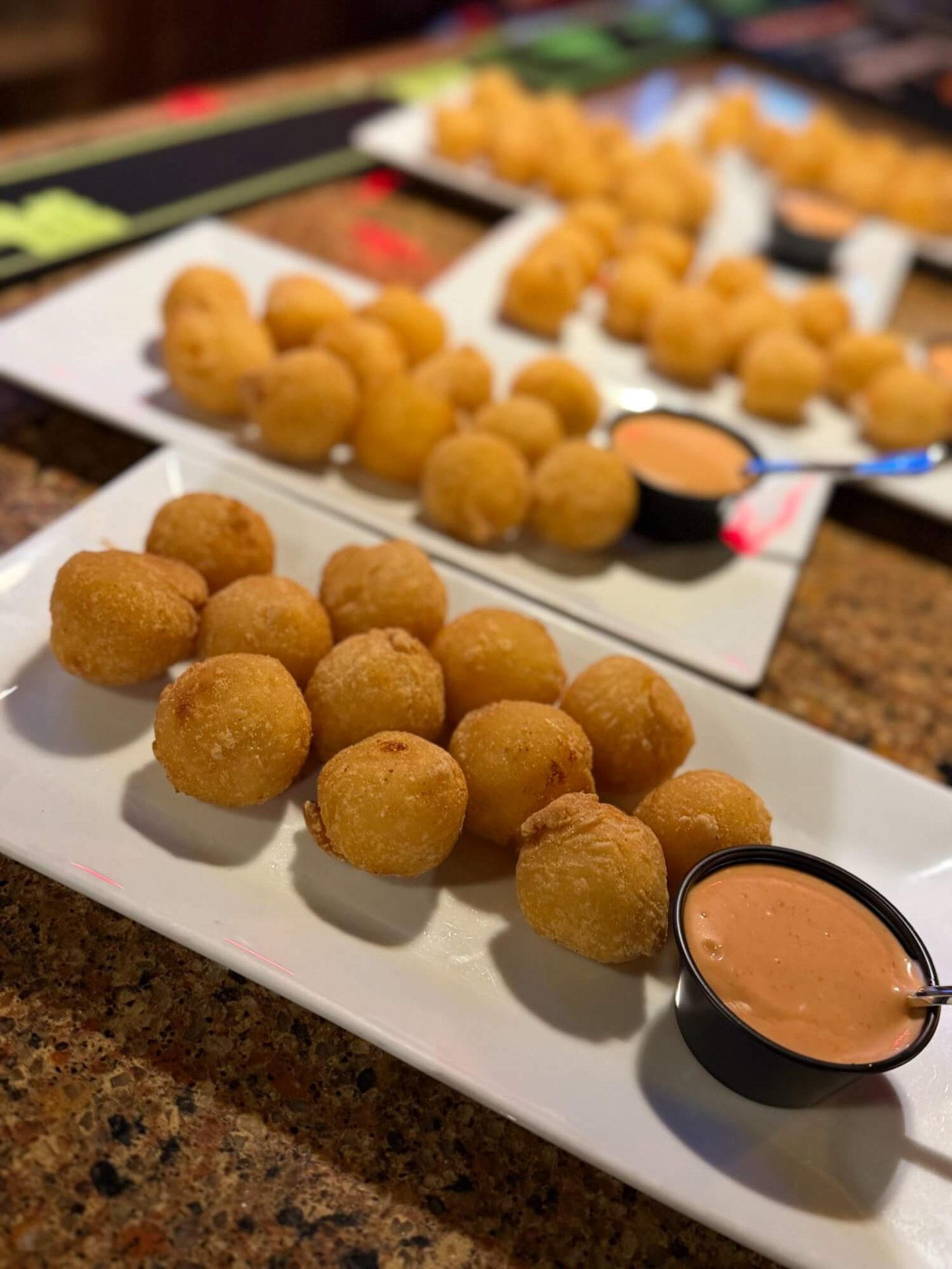 Rows of fried cheese balls are arranged on white rectangular plates, each served with a side of creamy orange dipping sauce.