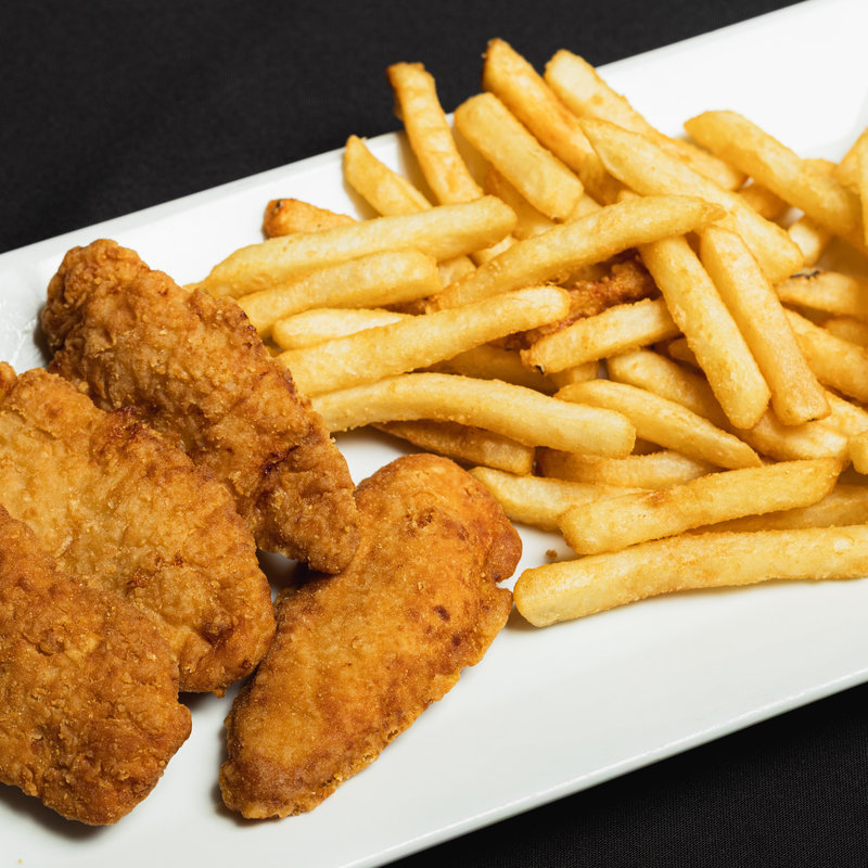 A rectangular white plate with three breaded chicken tenders and a serving of golden French fries on a black background.