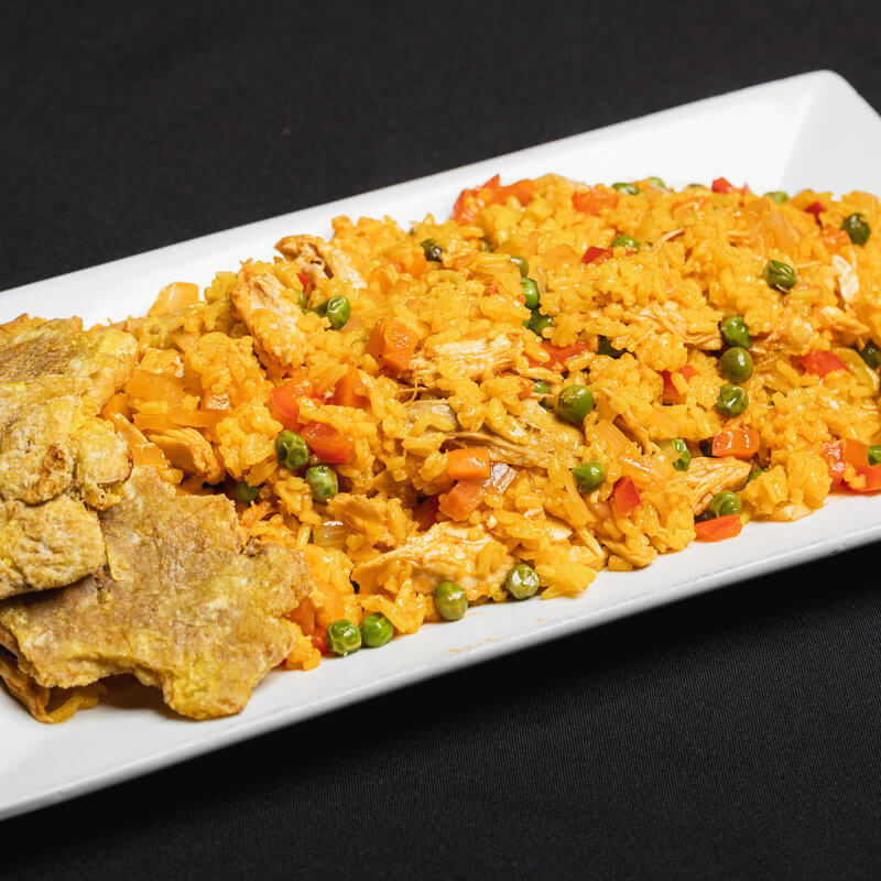 Rectangular white plate with yellow rice mixed with vegetables and chicken, served alongside several pieces of fried plantain, all on a black background.