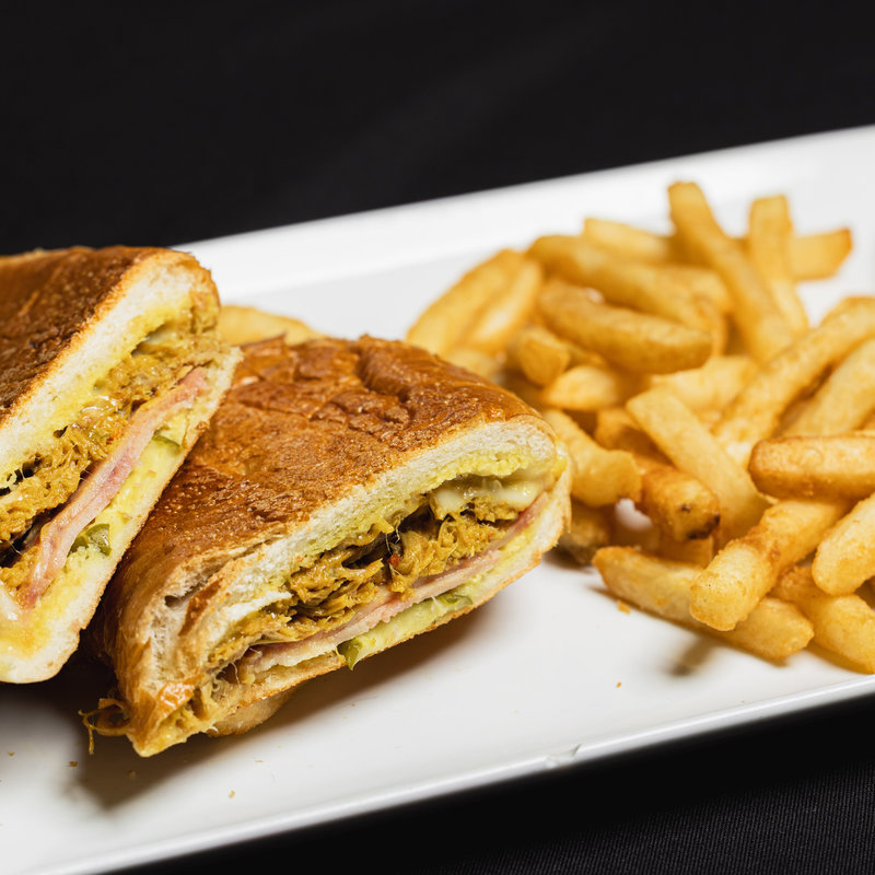 A pressed sandwich cut in half is served with a side of crinkle-cut French fries on a rectangular white plate against a black background.