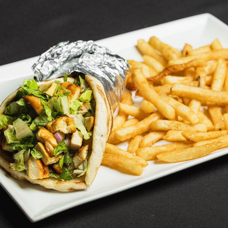 A chicken gyro wrapped in foil is served with lettuce, onions, and sauce on pita bread, alongside a portion of French fries on a white rectangular plate.