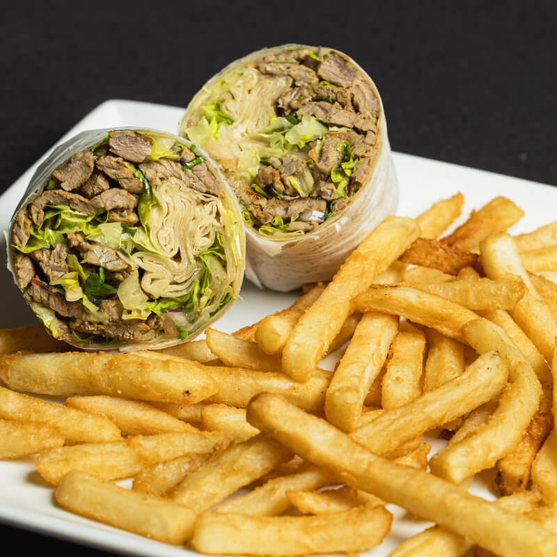 A wrap filled with lettuce and grilled meat, sliced in half, is served on a white plate with a side of golden French fries.