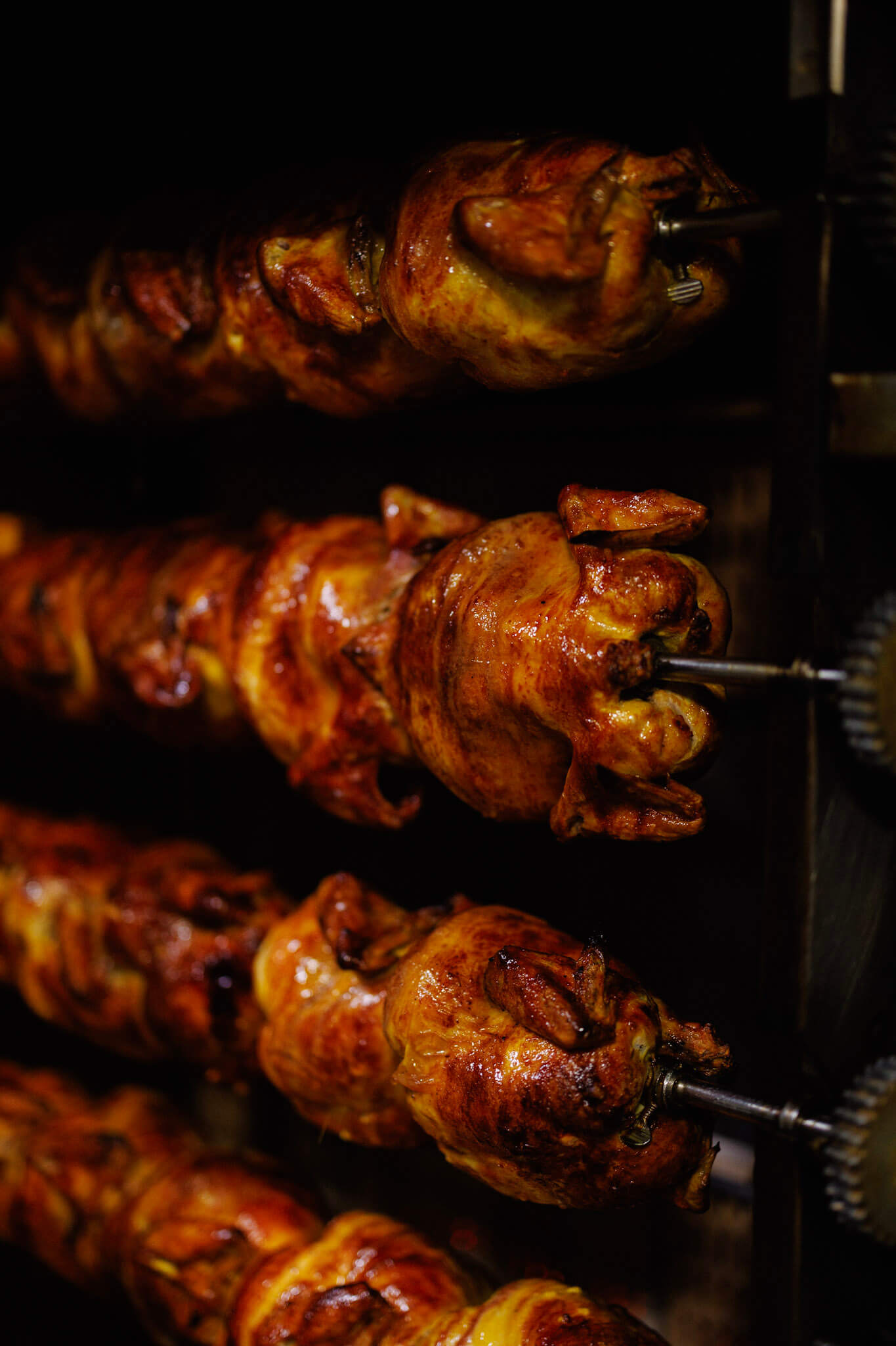 Rows of whole chickens roasting on metal spits inside an oven.
