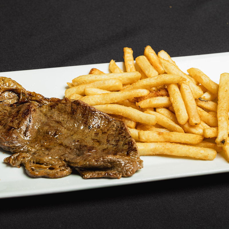 A grilled steak and a serving of French fries are arranged side by side on a rectangular white plate, set against a black background.